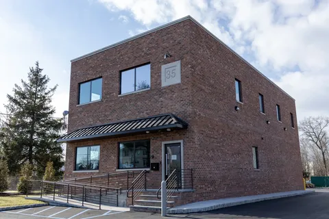 Two-story red brick office with a dark metal awning, a stone 35 plaque and an accessible ramp to the entrance