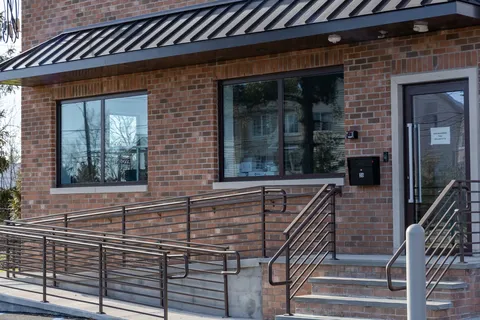 Office entrance with a glass door, two picture windows, and a dark metal railing along the ramp and steps