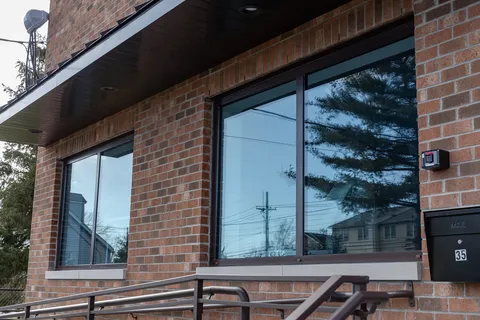 Dark-framed windows in the brick facade, reflecting a pine tree, utility lines and neighboring houses