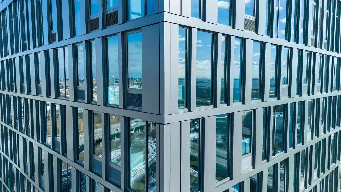 Corner of the glass facade at Atlas on Johnston Avenue in Jersey City, its panes reflecting the sky, the harbor and a highway interchange